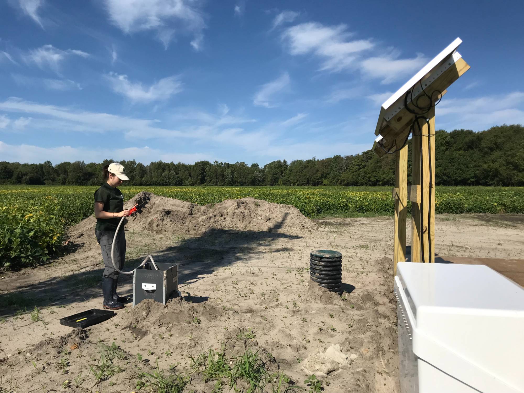 A field technician stands at the edge of a farm field and uses a sonde to measure water quality.